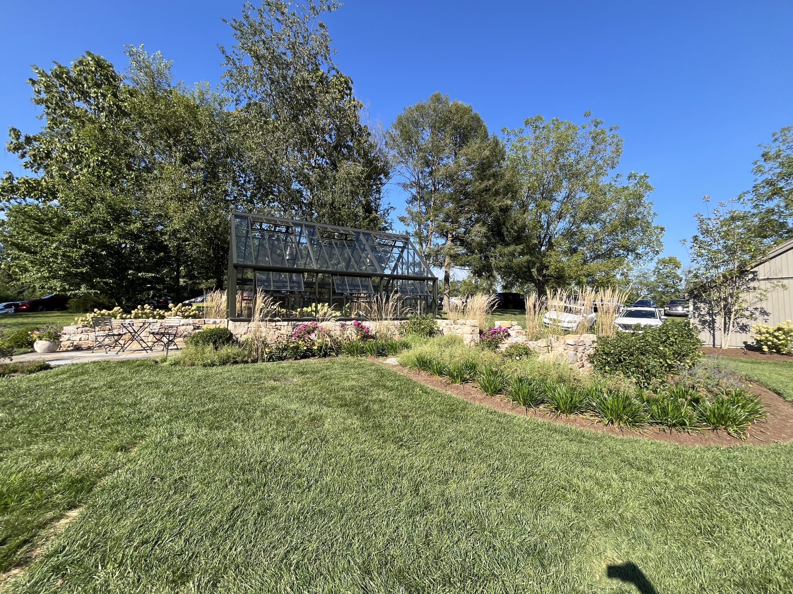 Glass greenhouse surrounded by garden and trees.