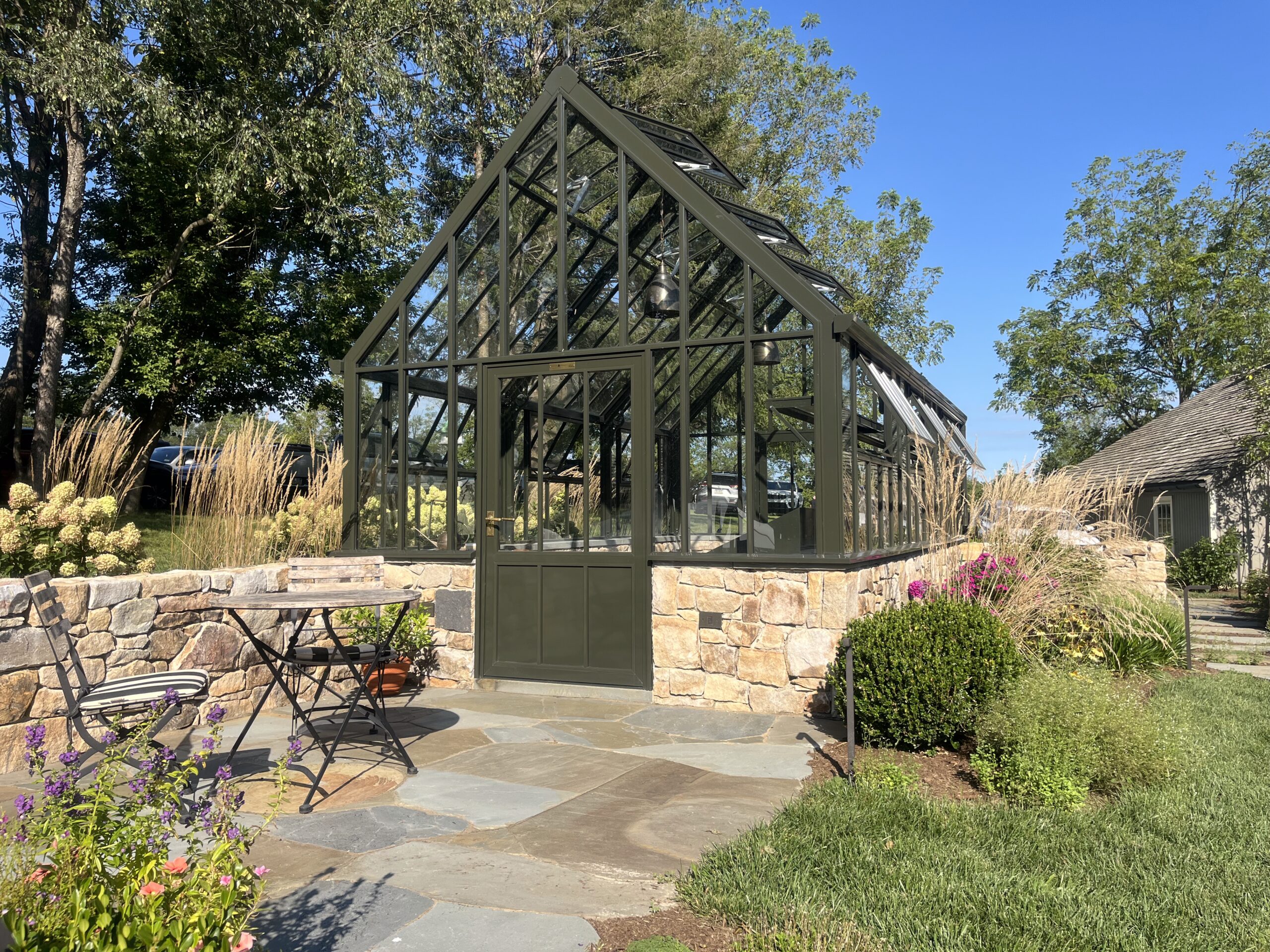 Modern glass greenhouse in landscaped garden setting.
