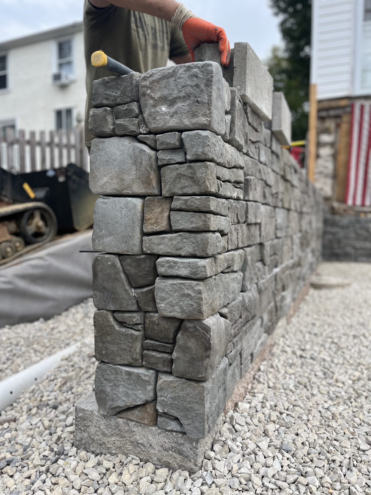 Builder constructing stone wall on gravel base.