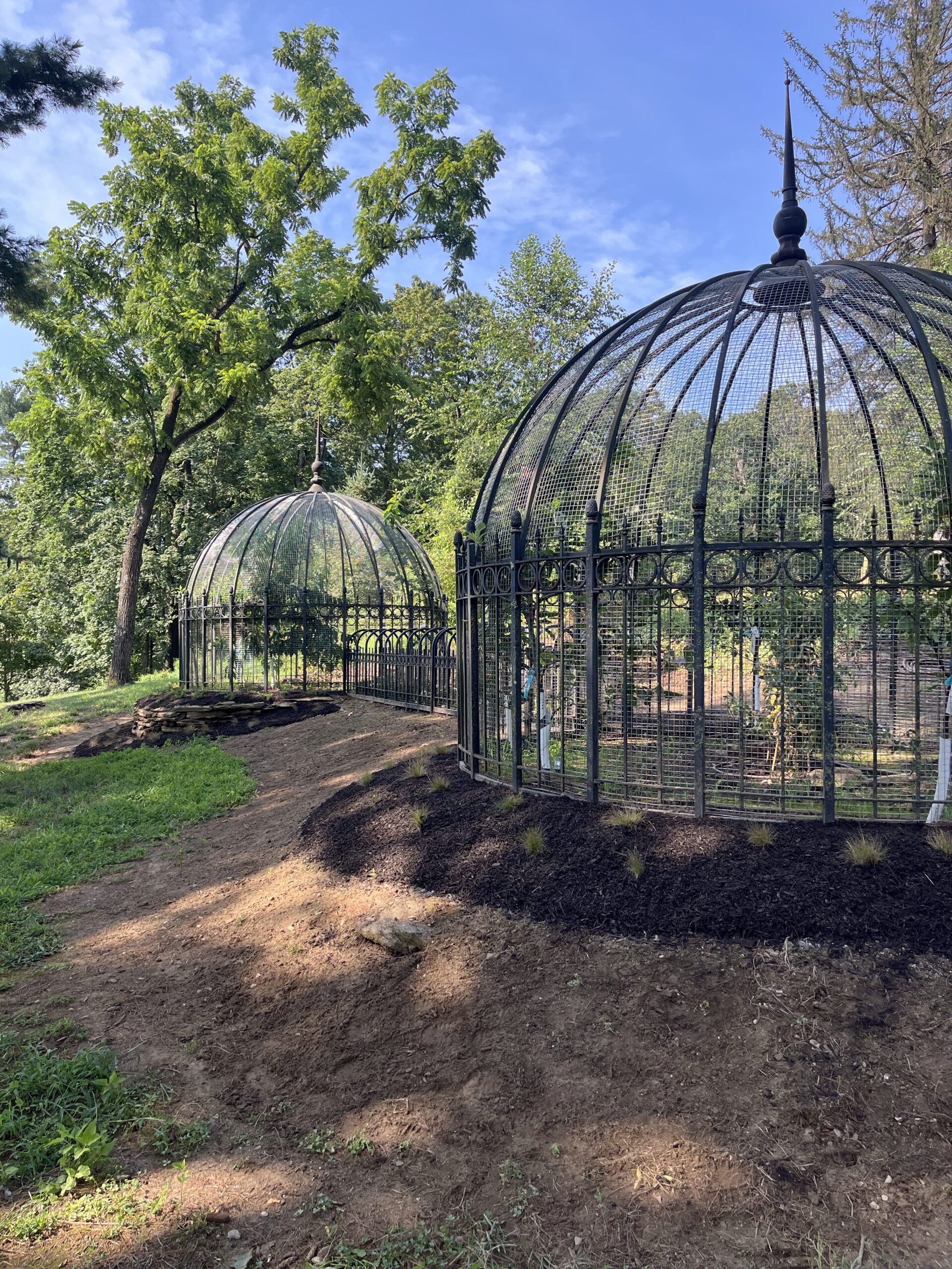 Outdoor garden with large birdcages and trees.