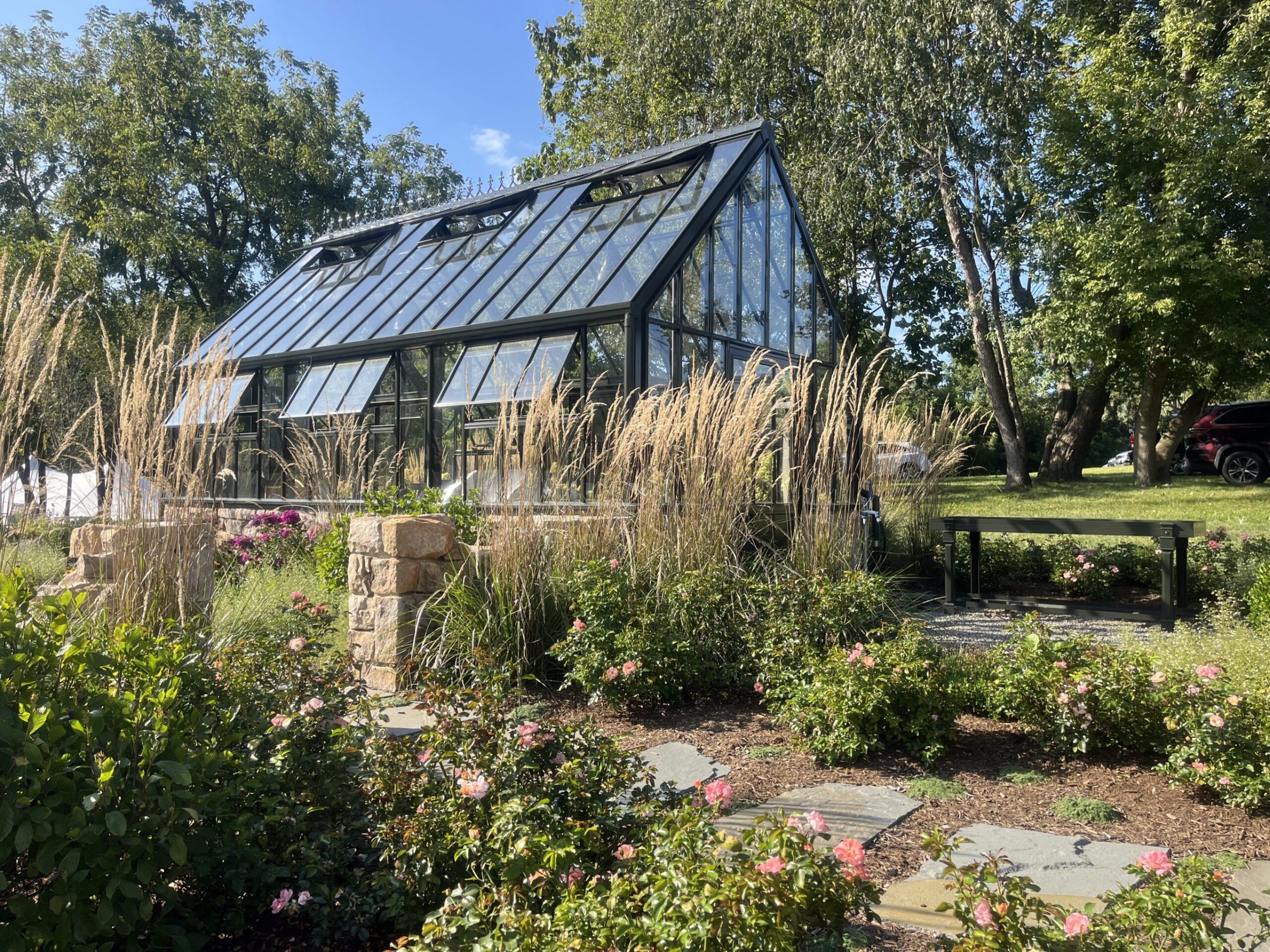 Greenhouse in garden with tall grass and flowers.
