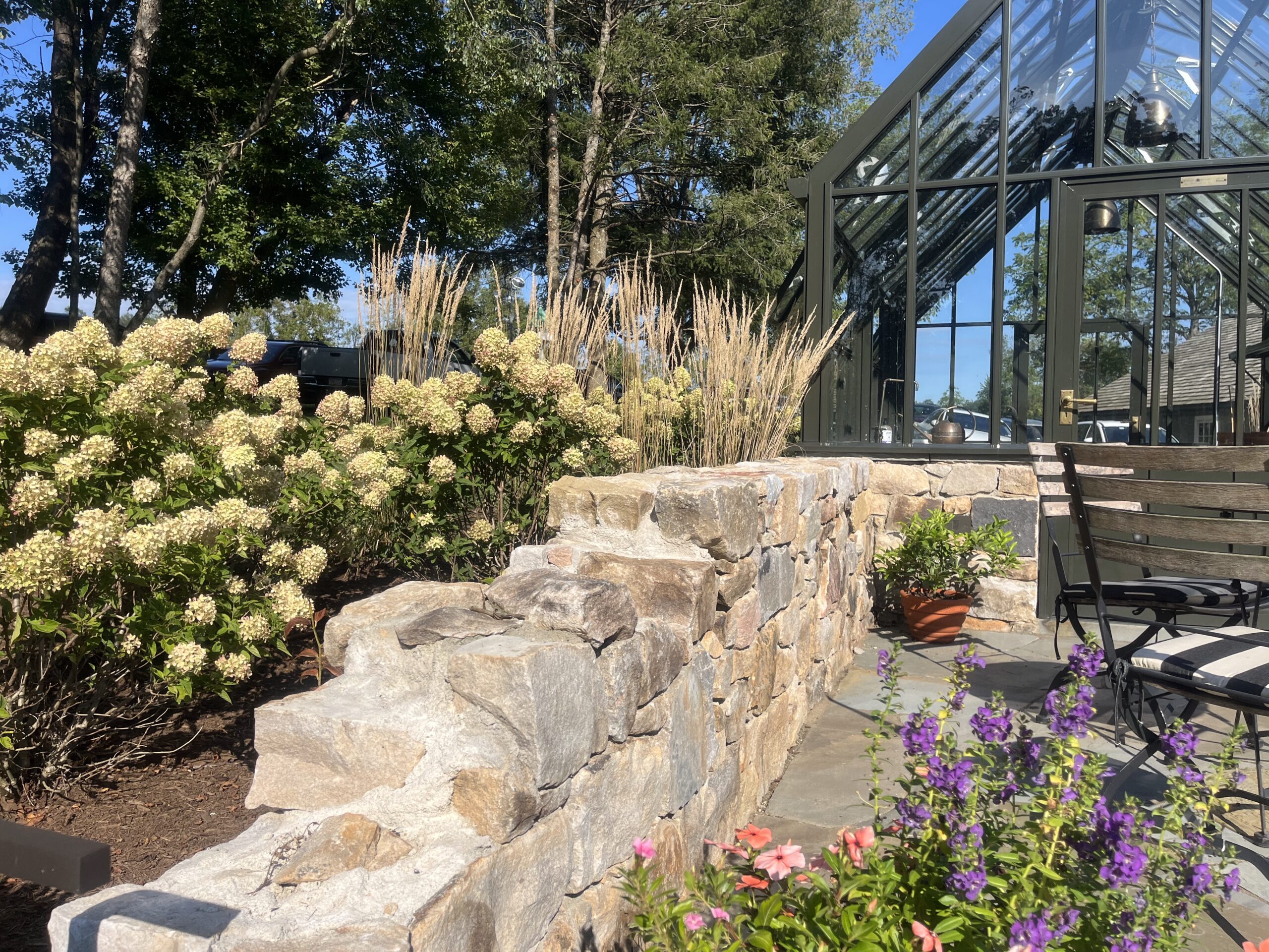 Stone wall and garden by glass greenhouse.