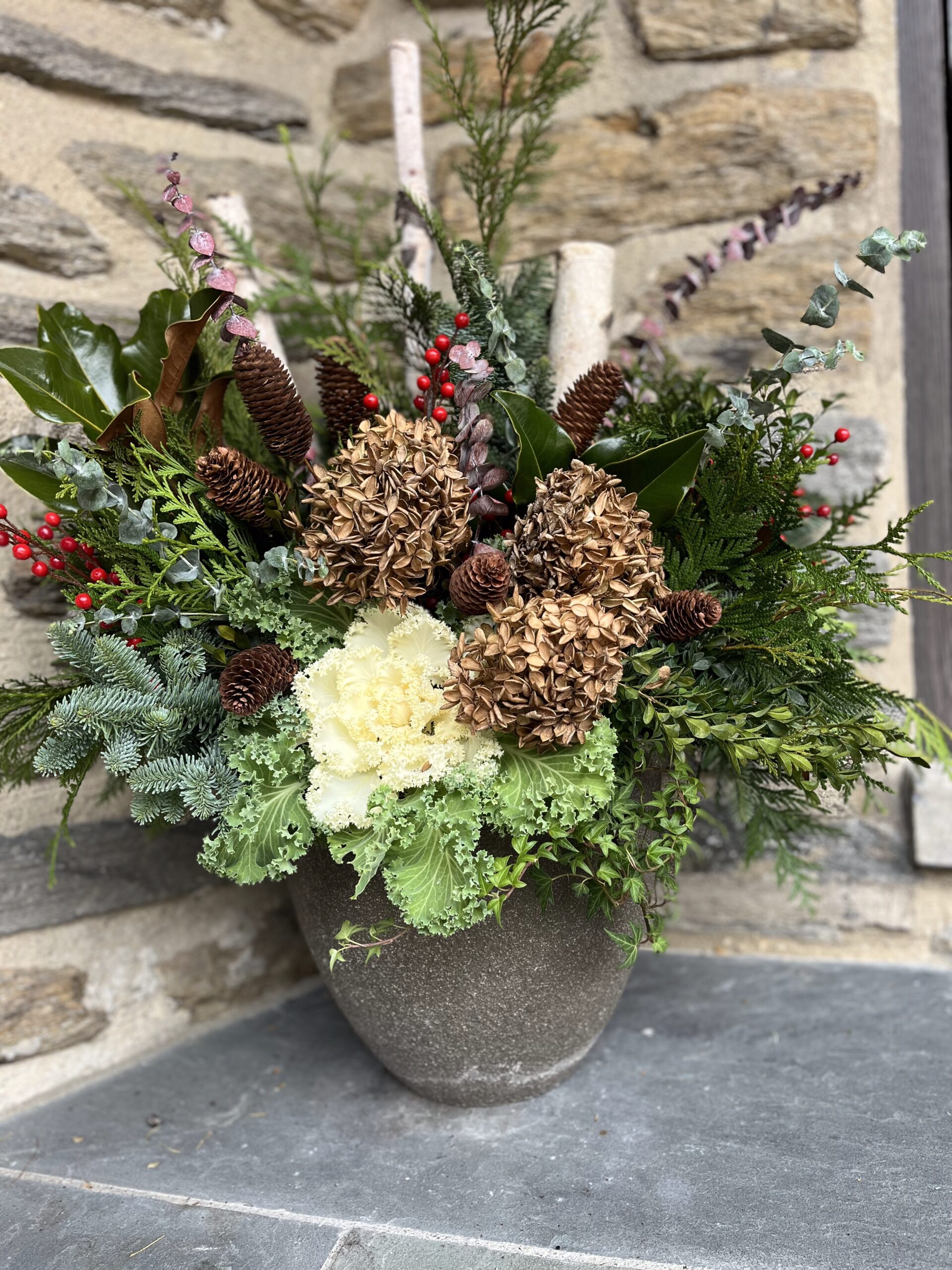 Rustic floral arrangement with pinecones and greenery.