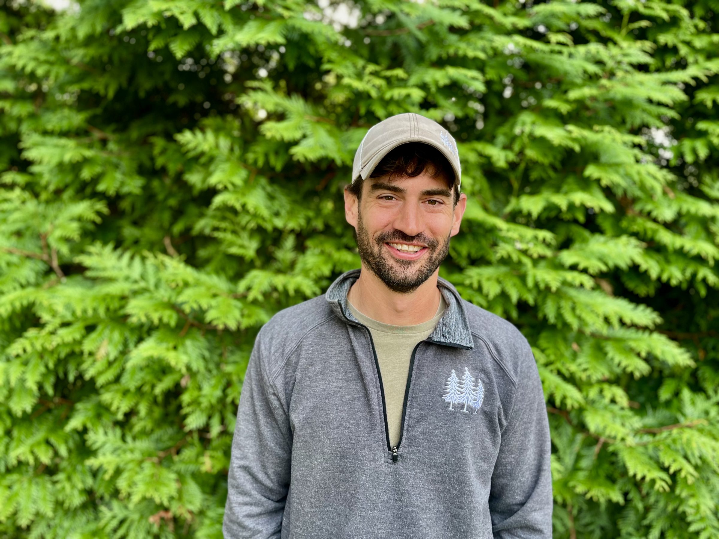 Man smiling in front of green leafy background.