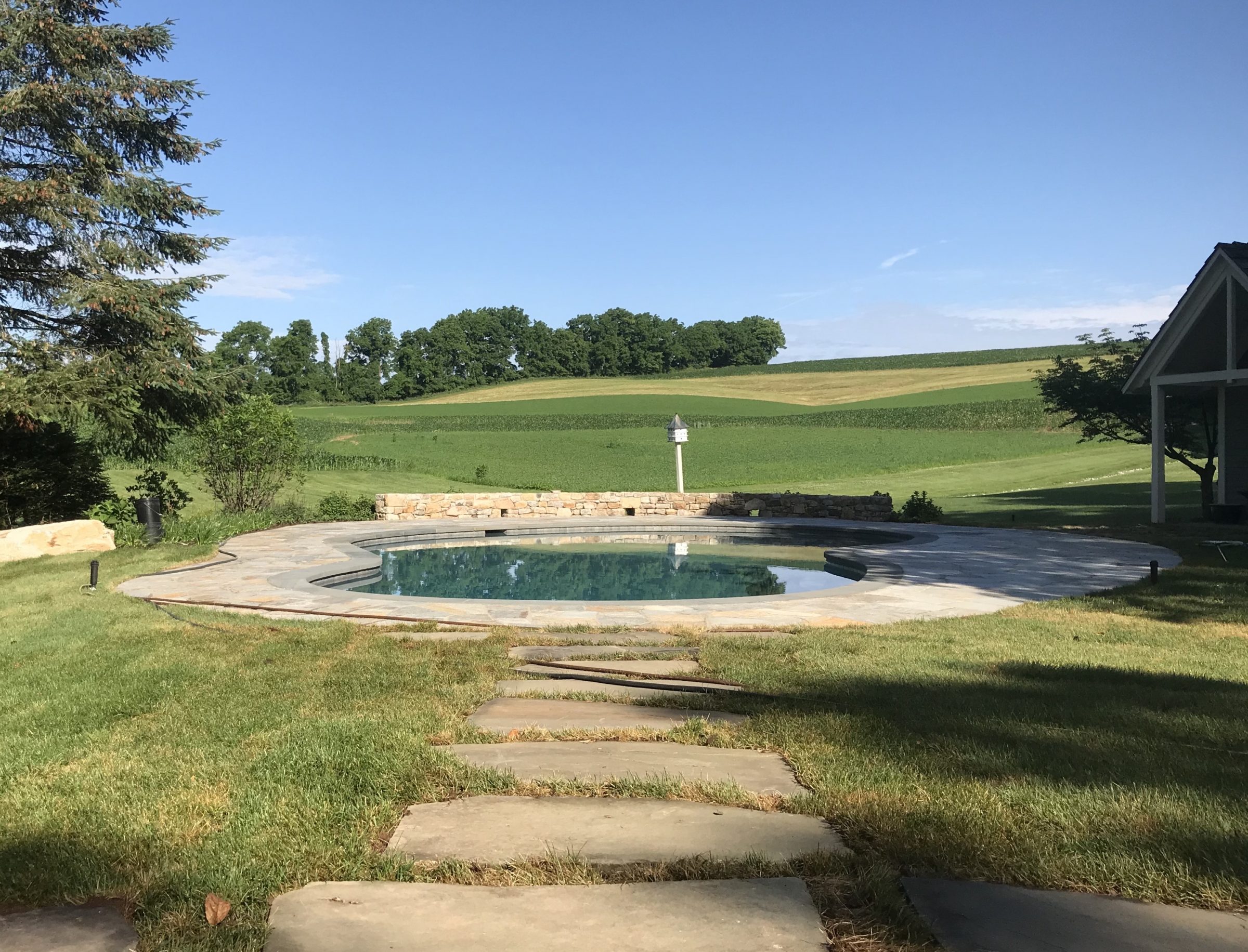 Circular pool with stone path, rural landscape view.